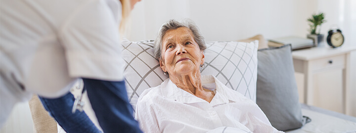 A young health visitor talking to a happy sick senior woman lying in bed at home.