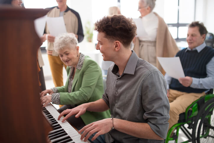 senior woman with young teacher playing piano at an assisted living facility