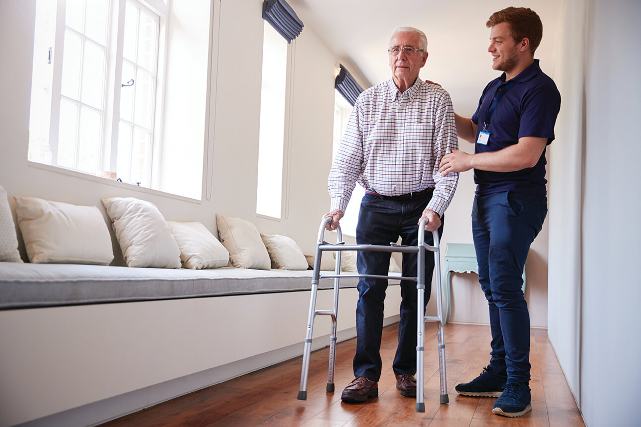 Senior woman using a walking frame with male nurse at home